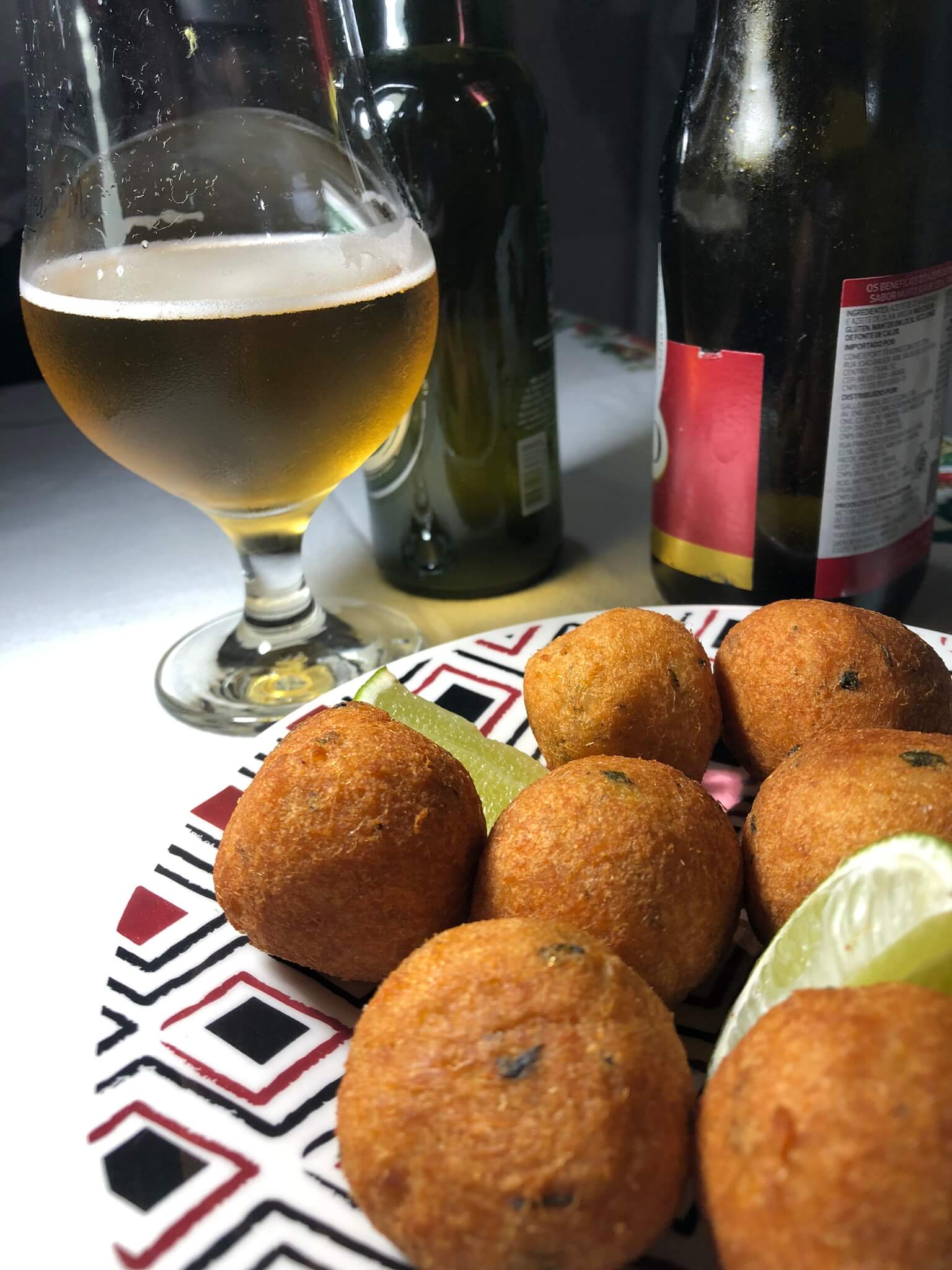 Um prato de bolinhos de bacalhau com uma taça de cerveja ao fundo