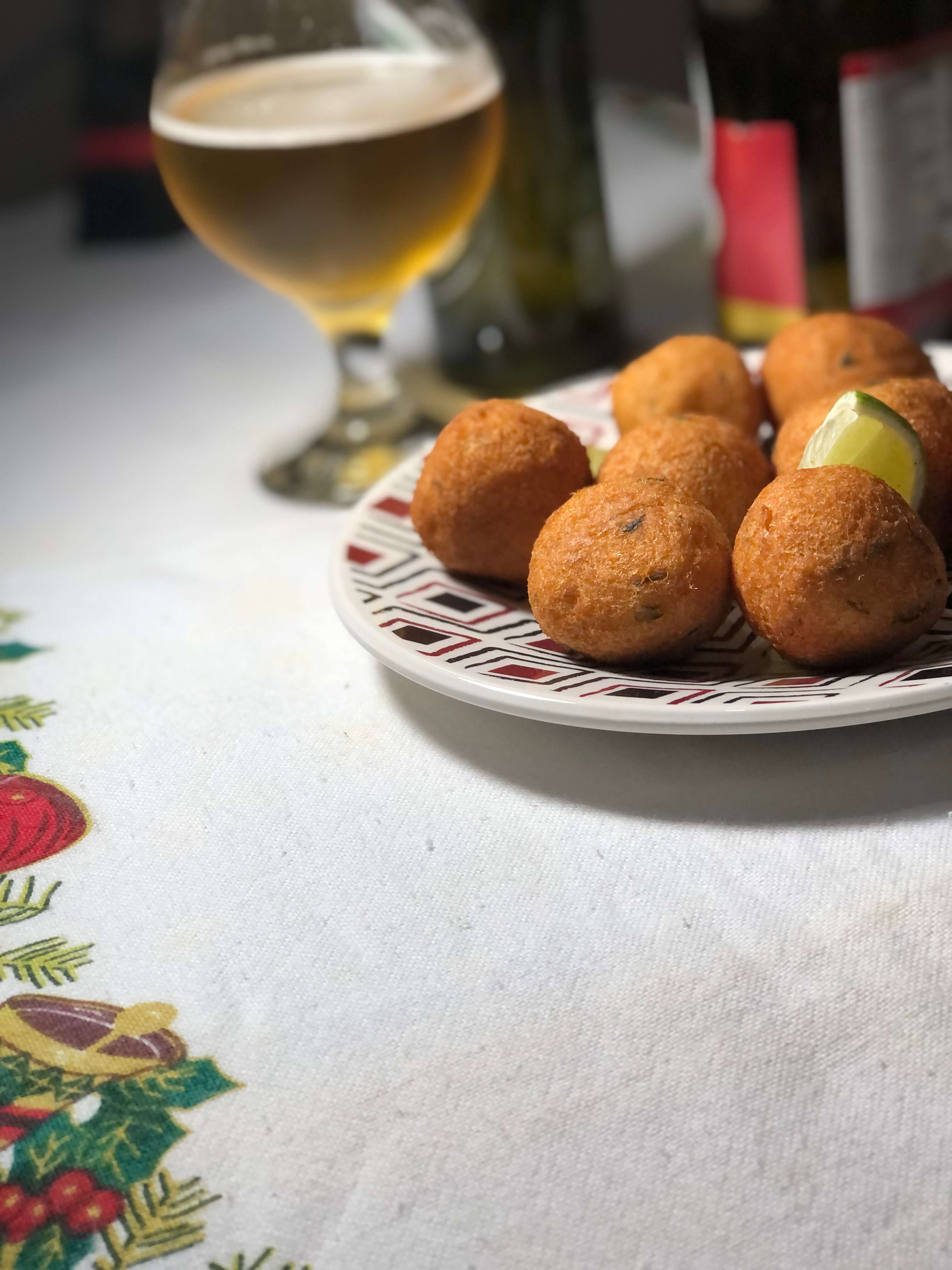 Mesa com um prato de bolinhos de bacalhau e uma taça de cerveja no fundo